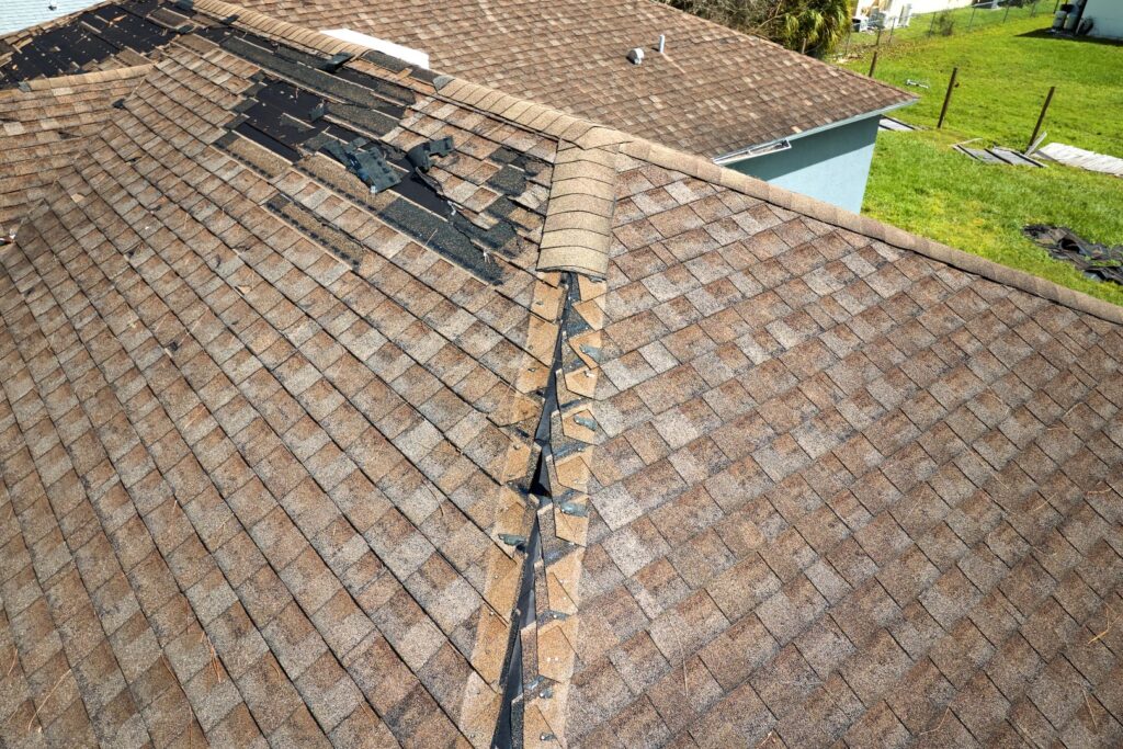 Damaged roofing shingles with missing and lifted sections.