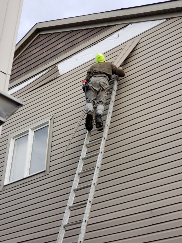 Technician performing siding repair on a two-story home.