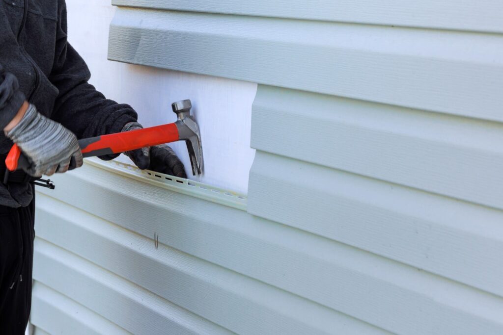 Technician replacing a damaged vinyl siding panel with a hammer during siding repair.